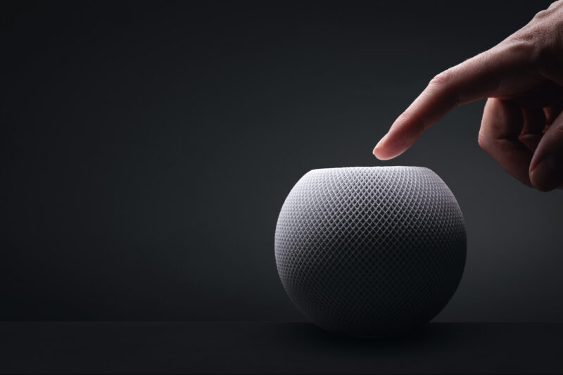 Apple HomePod mini with a hand on dark background