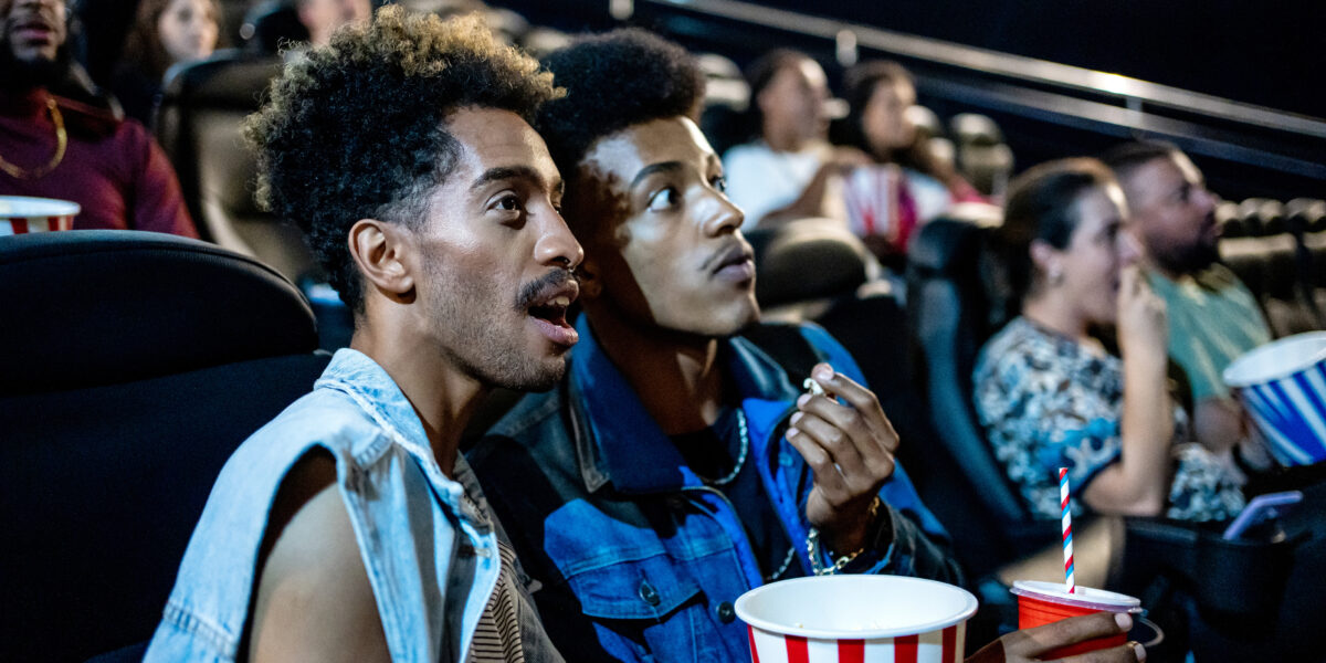 Two men eating popcorn while watching a movie