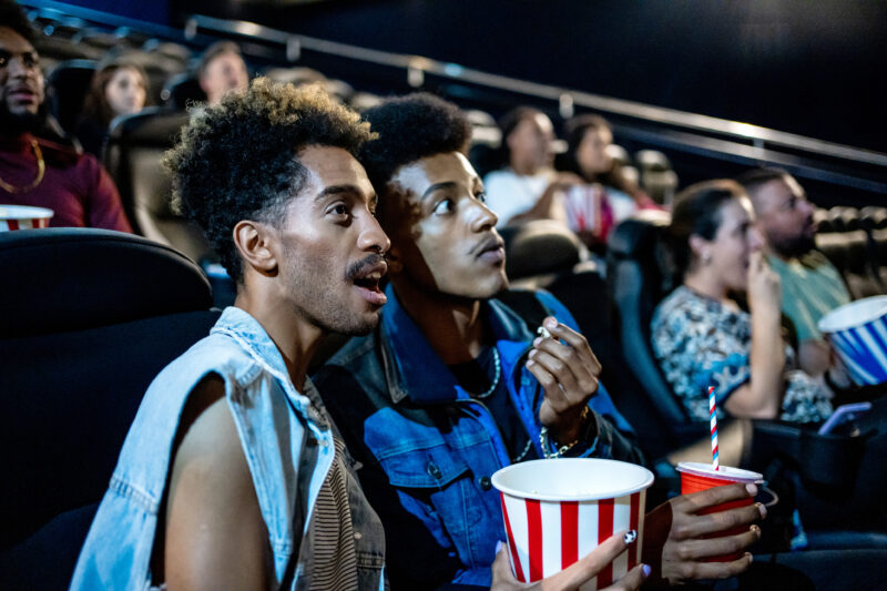Two men eating popcorn while watching a movie