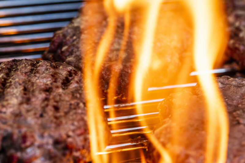 Close-up of beef patties, cooking on a kettle charcoal grill