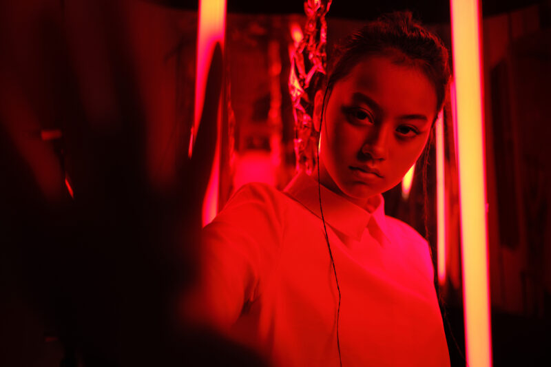 Portrait of young asian teenage girl with hand towards the camera, in red neon light.